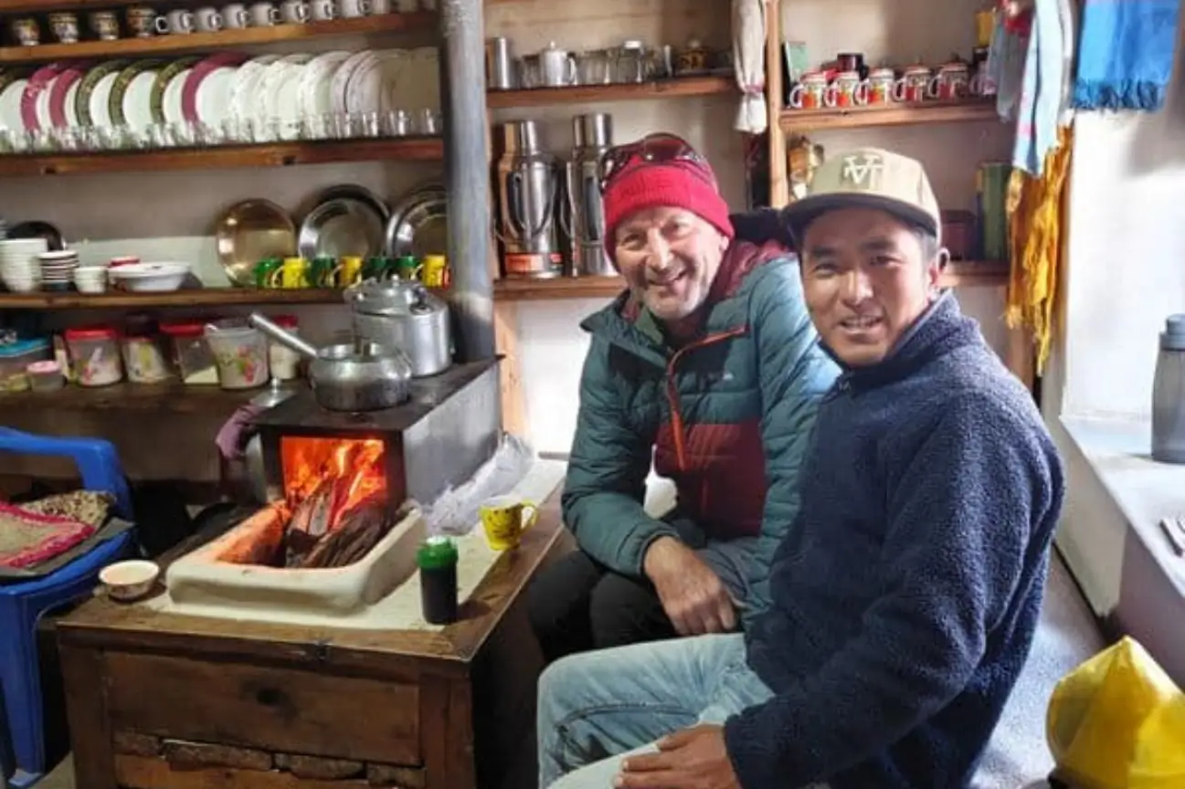 Trekkers smiling and warming up near a cozy indoor fireplace featured in the Annapurna Circuit Trek Guide.