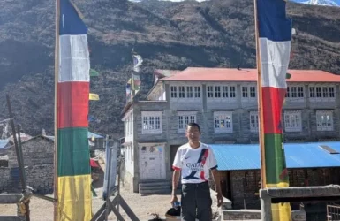 Annapurna Circuit Trek Guide Lakeside Treks Trekker standing near colorful prayer flags and a mountain lodge featured in the Annapurna Circuit Trek Guide.